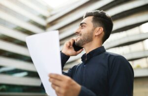 Arab entrepreneur man speaking on mobile phone holding papers outside