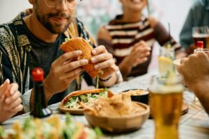 Close up of man eating tacos with his friends in a restaurant.