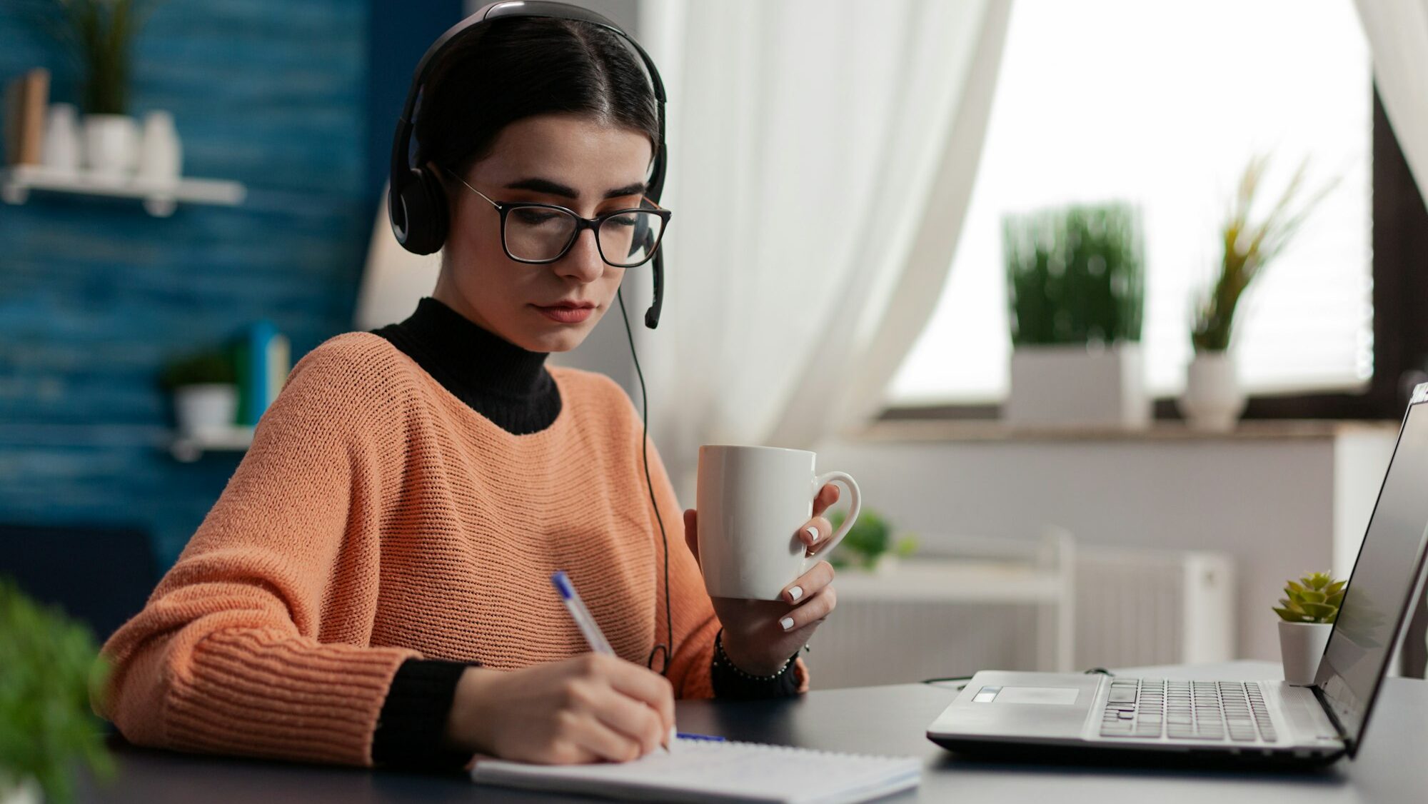 Student with headphones listening to online course and taking notes